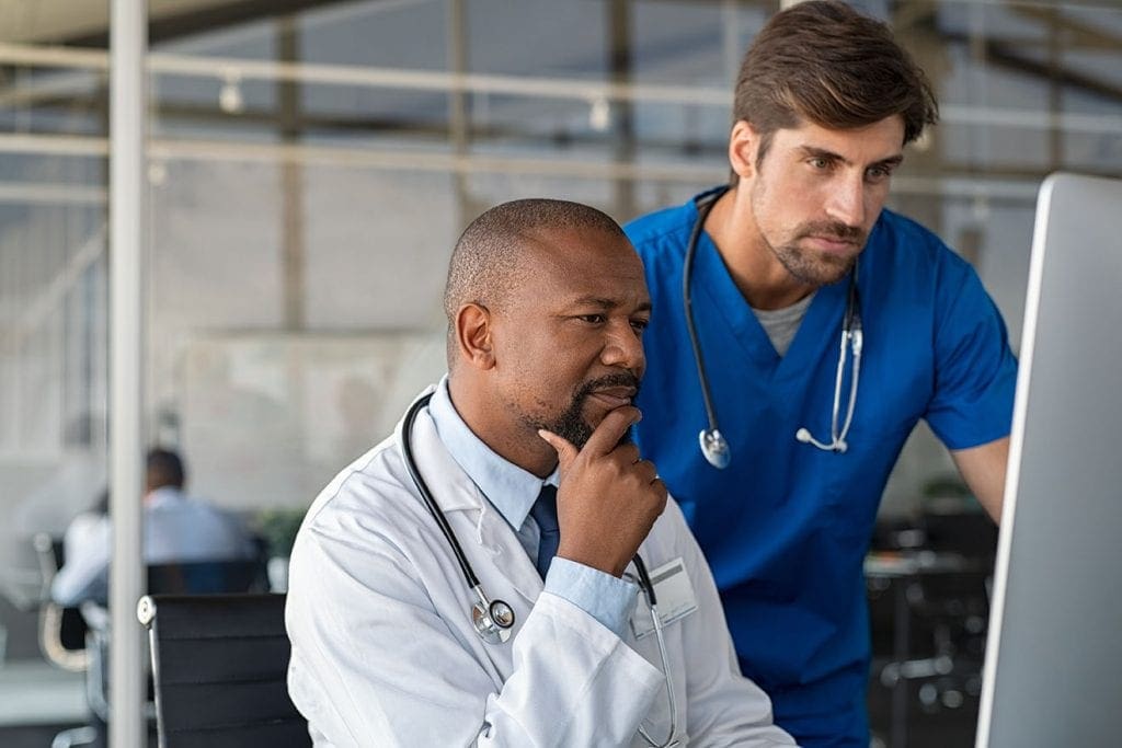 male doctor ling intently at electronic health record while male nurse also looks over his shoulder